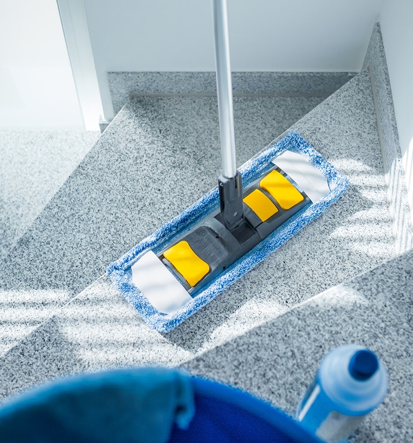 Nettoyage Sol Granit : Serpillière Microfibre Professionnelle Nettoyage d'escalier en granit avec une serpillière plate microfibre et un manche, près d'un seau et d'une bouteille de produit.