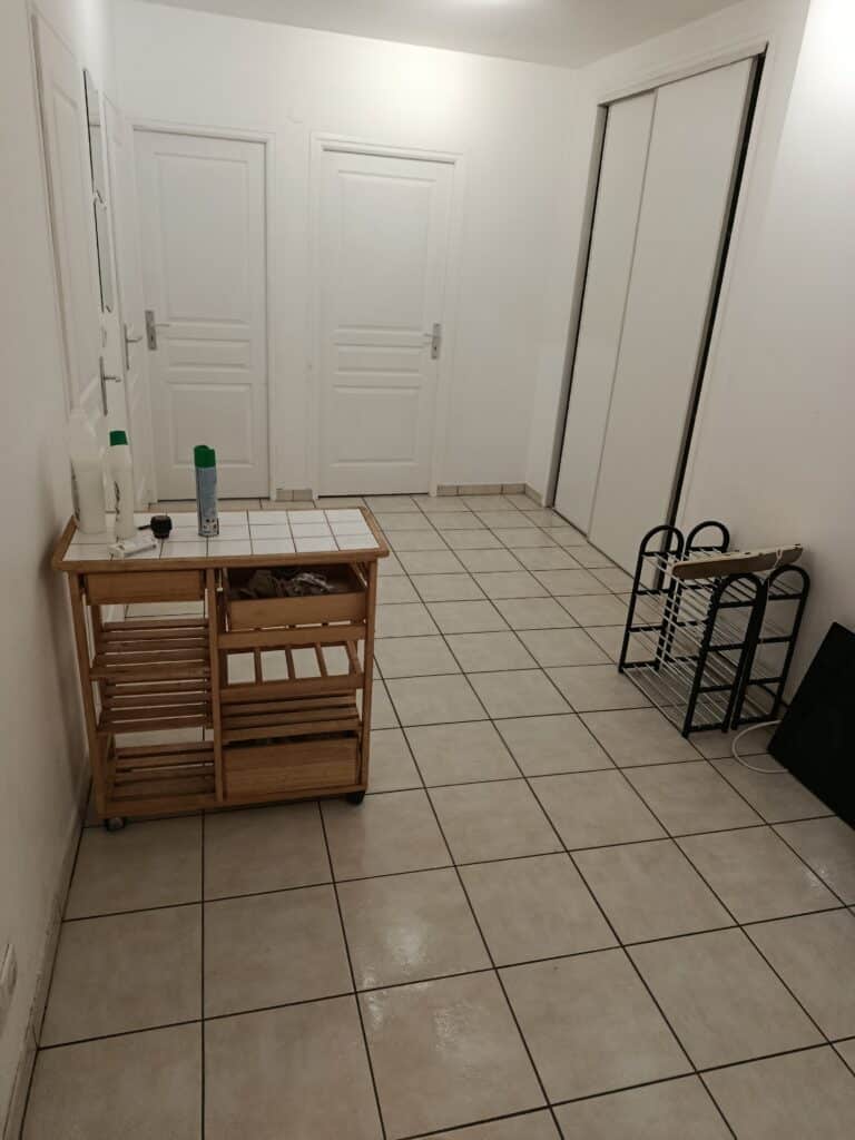 Hall d'entrée moderne: placard, carrelage et desserte optimisée. Couloir moderne: carrelage, murs blancs, deux portes, grand placard coulissant. Desserte en bois avec produits et étagère à chaussures.