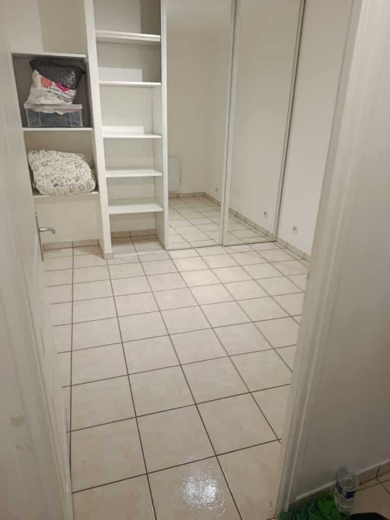 Rangement mural, étagères et placard miroir design. Dressing avec étagères et placard miroir dans un couloir carrelé. Le sac sur l'étagère dit : "Le vrai luxe c'est de faire croire à tout..."