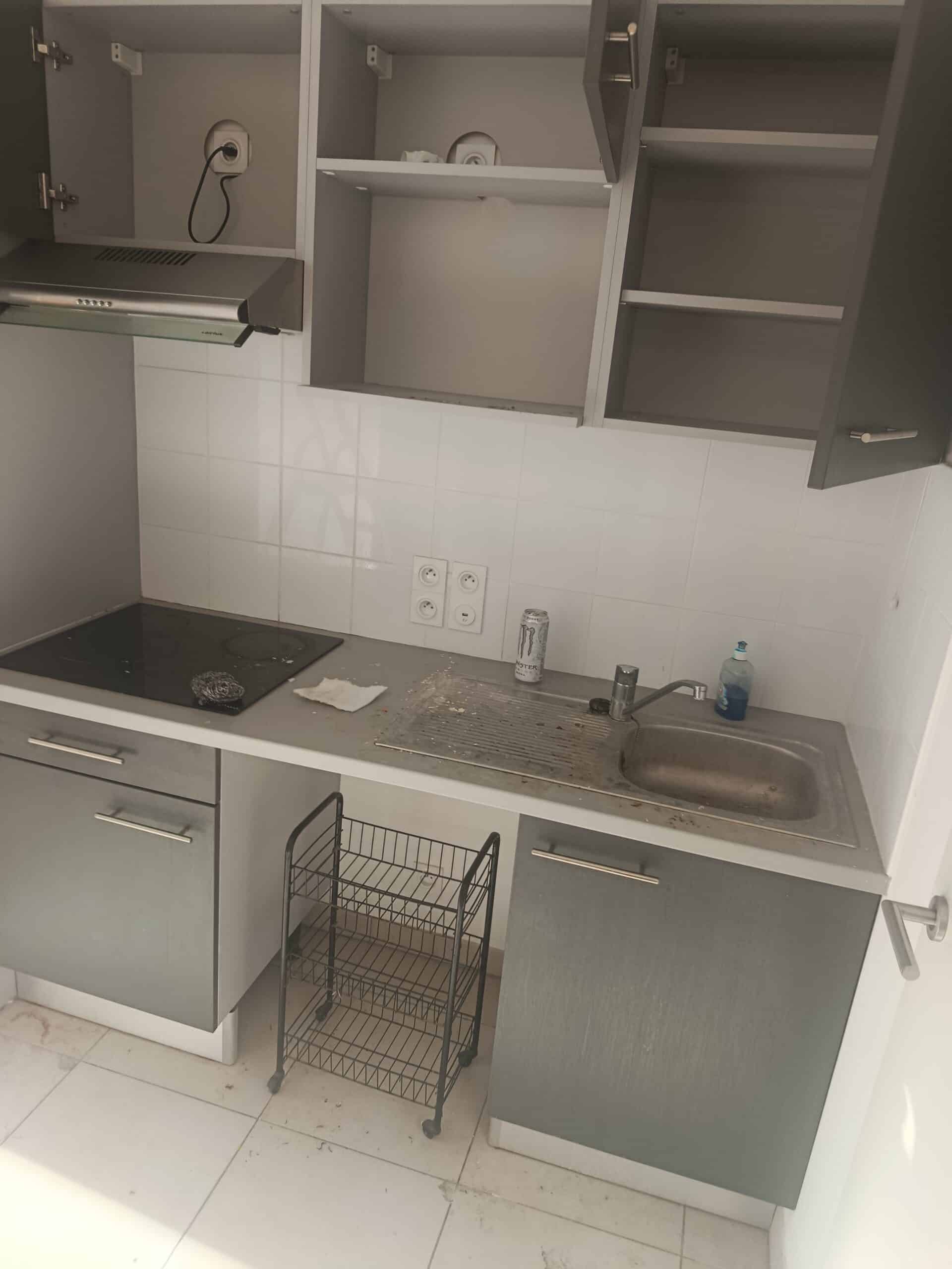 Petite kitchenette moderne avec placards gris, crédence blanche, plaques de cuisson noires et évier en inox.