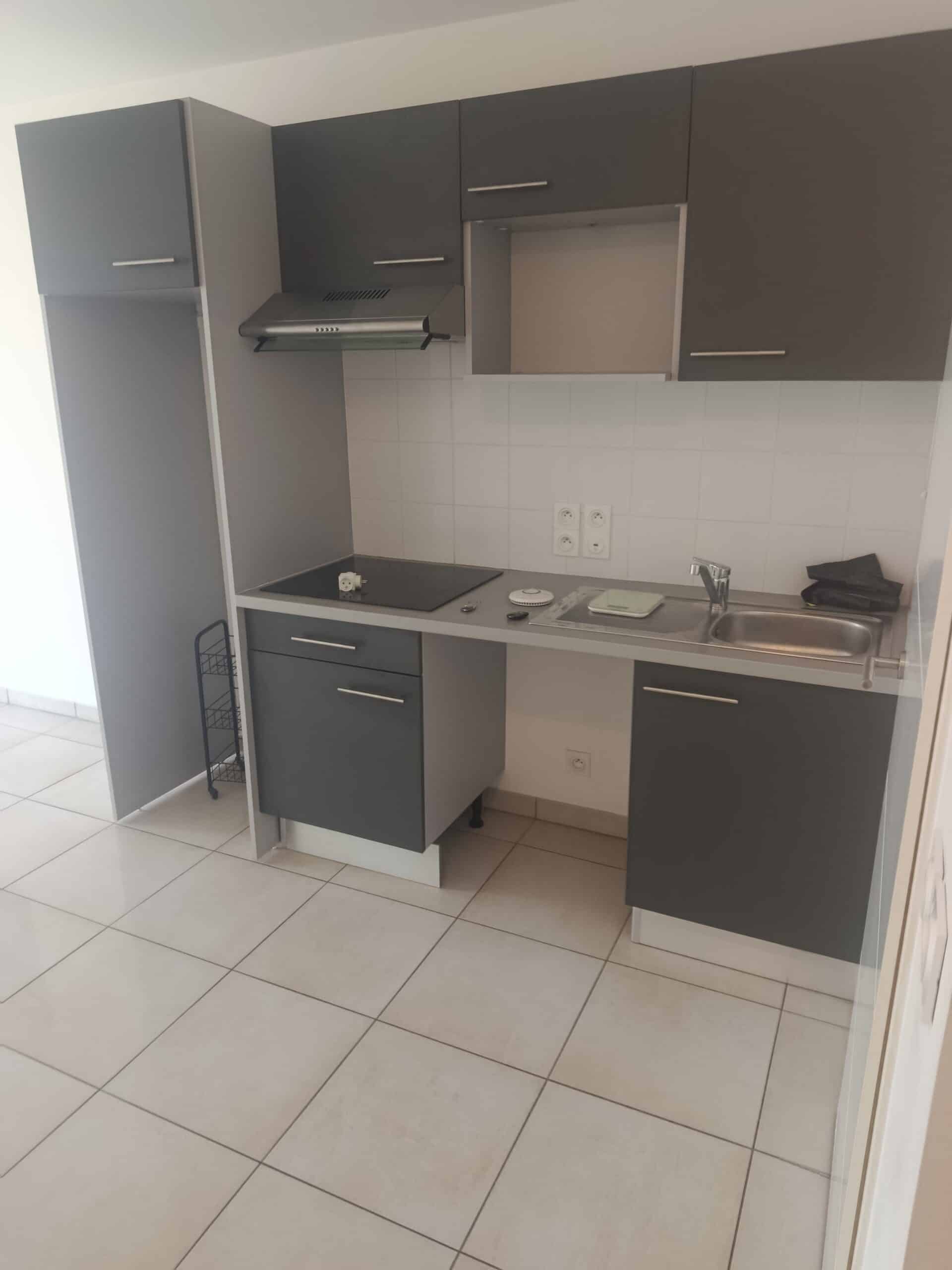 Kitchenette moderne avec meubles gris anthracite, plaque induction et évier sur carrelage clair.