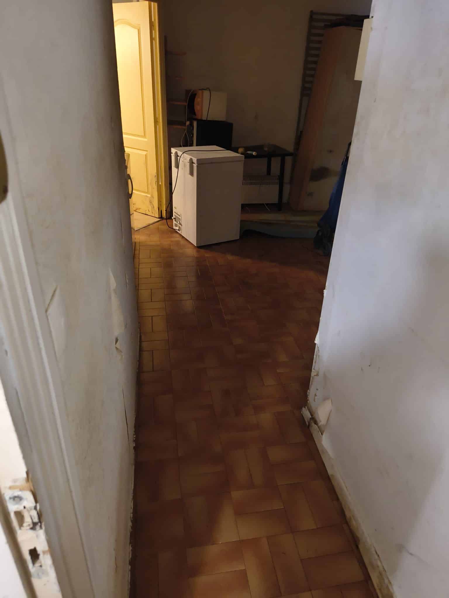 Petit congélateur blanc sur carrelage marron dans une pièce aux murs blancs abîmés.