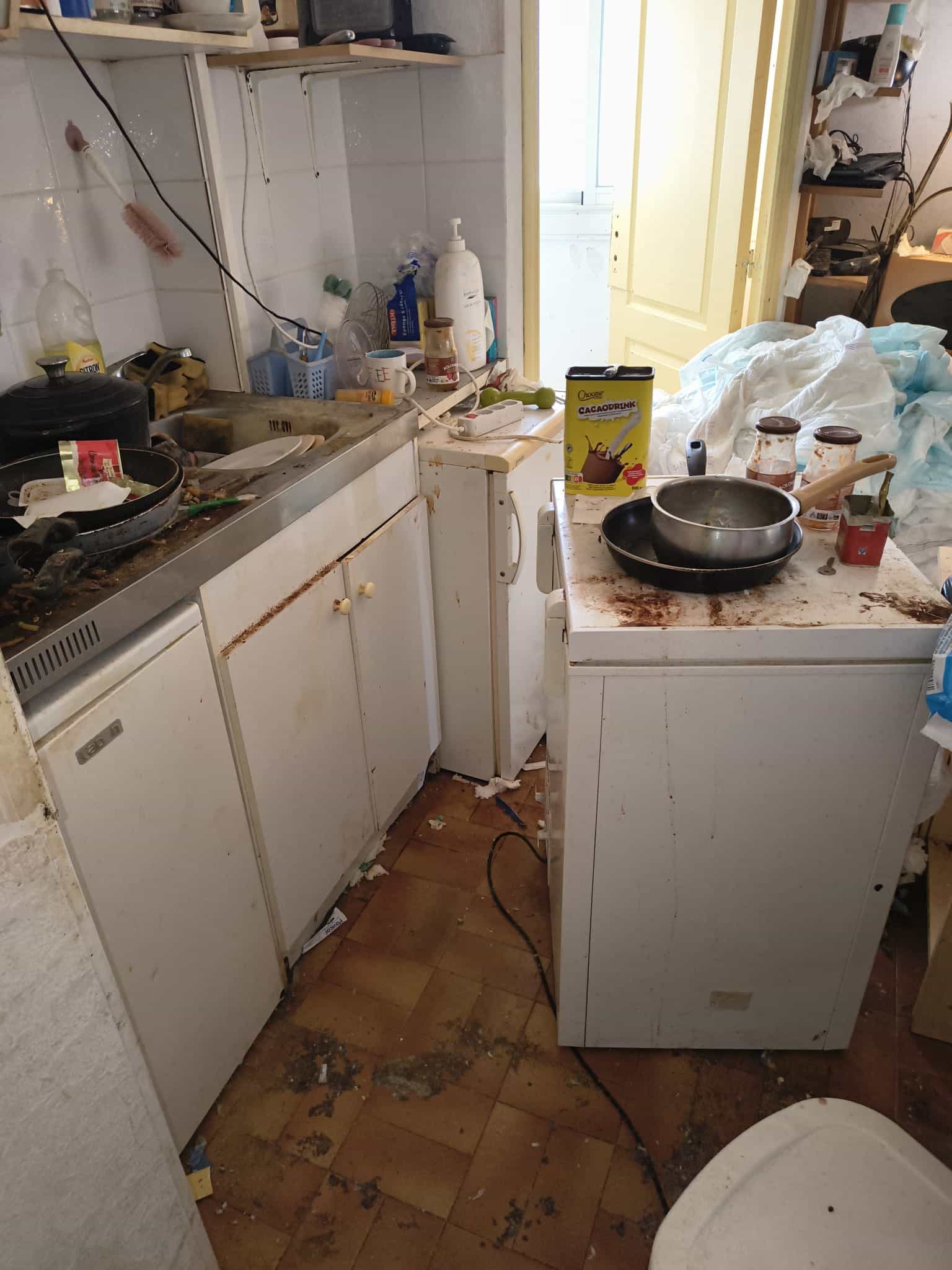 Cuisine insalubre, évier plein, plans de travail tachés, déchets et boîte de Cacaodrink.