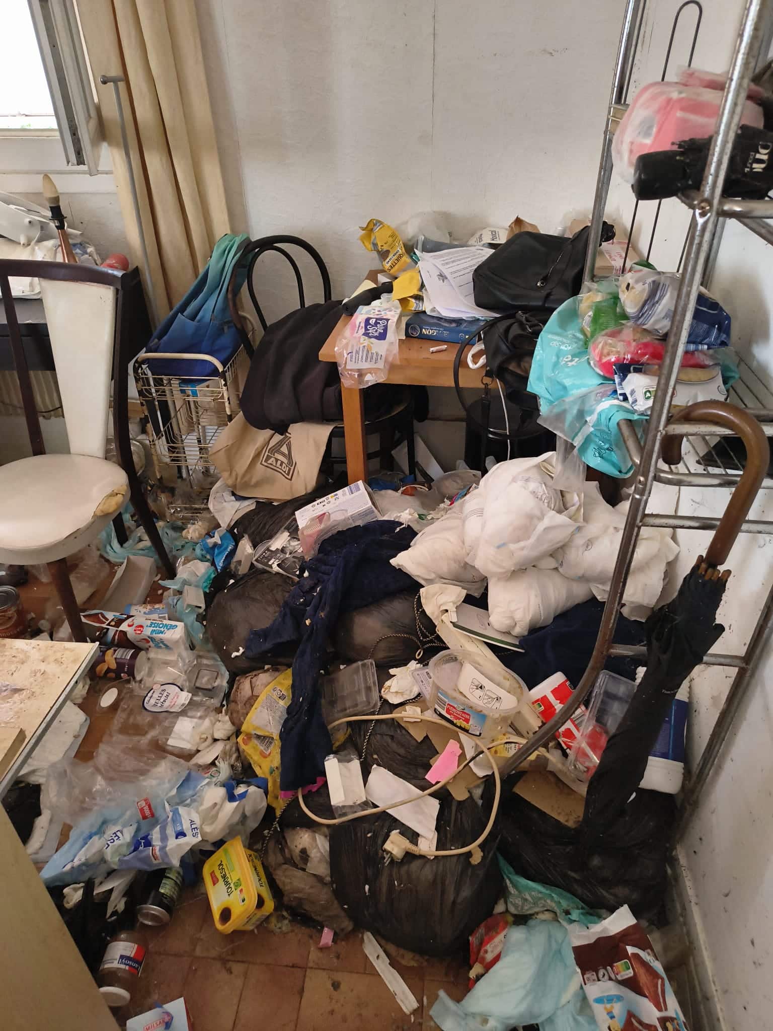 Logement insalubre saturé de déchets, sacs et emballages Aldi au sol. Accumulation extrême et désordre massif.