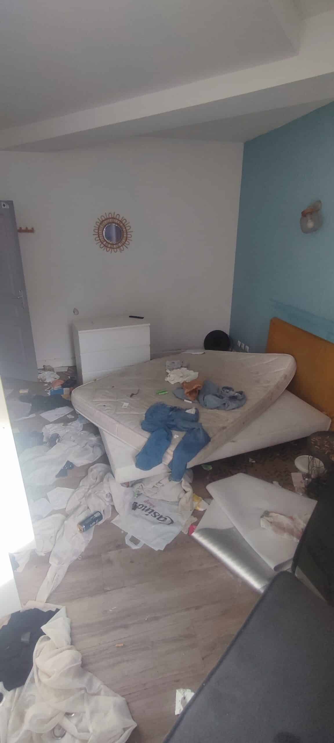 Chambre en désordre avec matelas au sol, vêtements éparpillés et déchets. Sac Casino Shop visible par terre.