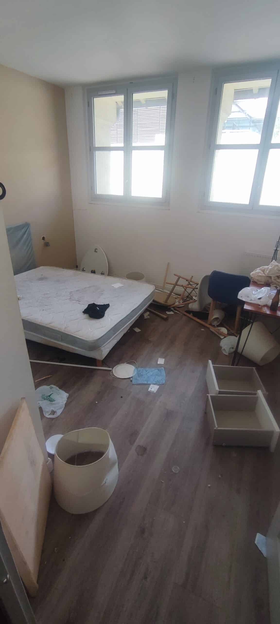 Chambre en plein désordre avec matelas taché, tiroirs au sol et meubles cassés dans un appartement à débarrasser.