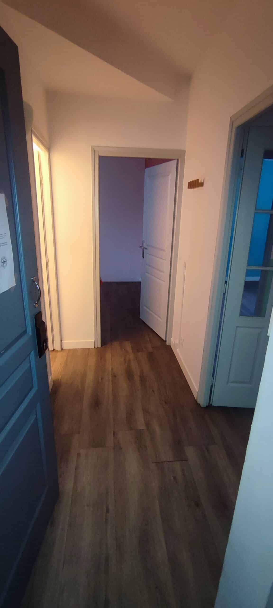 Couloir d'appartement moderne avec sol en parquet bois et portes ouvertes vers des pièces lumineuses.