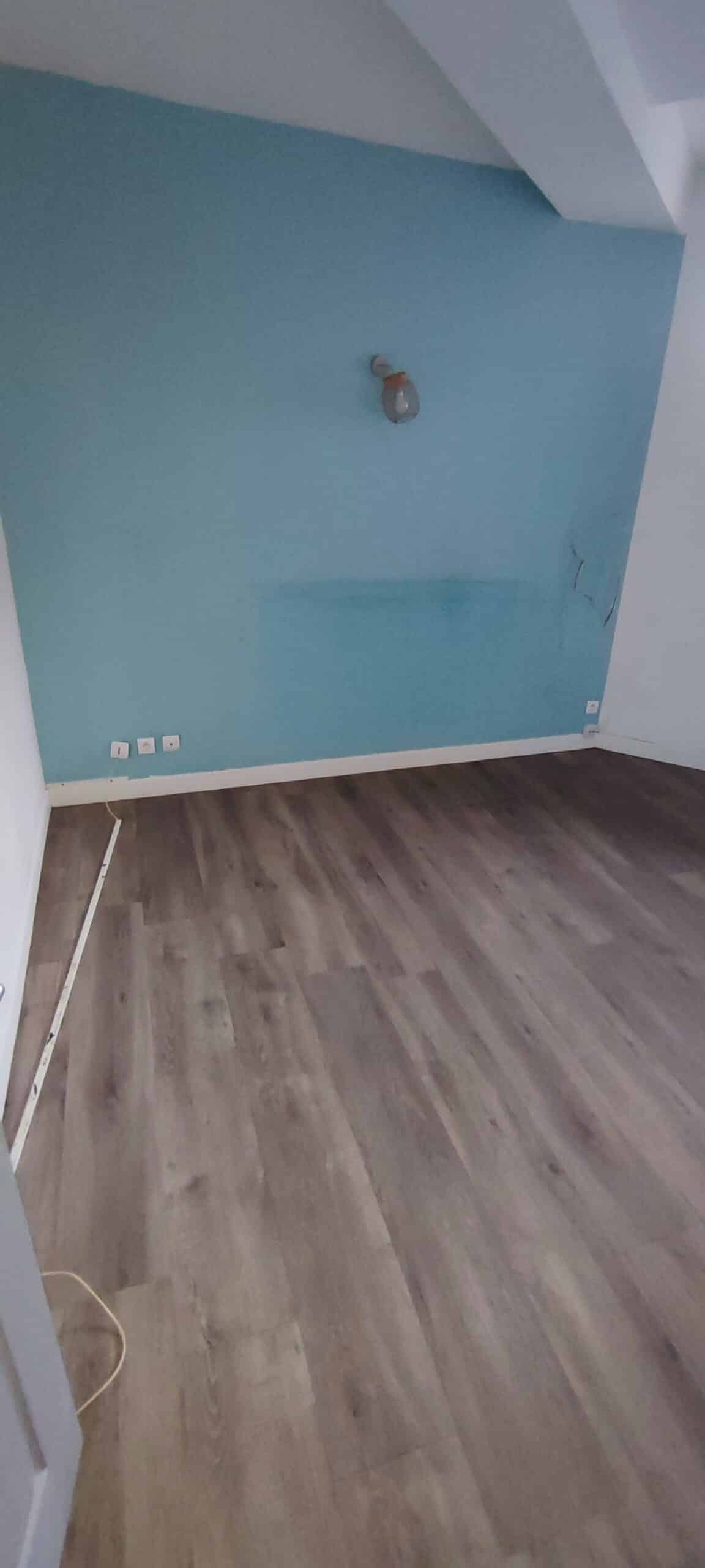 Mur bleu ciel, sol stratifié imitation bois et plinthes blanches dans une pièce vide en cours de rénovation.